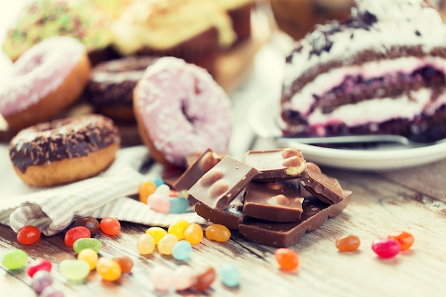 Foto junkfood, snoep en ongezond eten concept - close-up van chocoladestukjes, jelly beans, geglazuurde donuts en cake op houten tafel