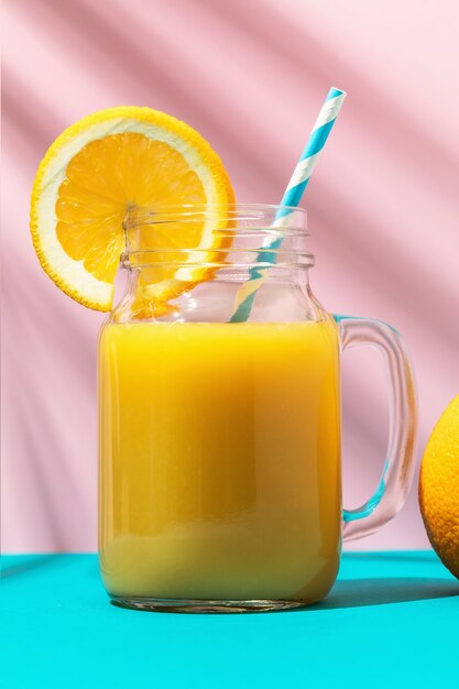 Jus d'orange in een glas met een rietje en een sinaasappel op een gekleurde achtergrond