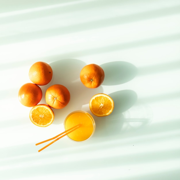 Foto jus d'orange in een glas omgeven door natuurlijke sinaasappels met een natuurlijke zon licht witte achtergrond