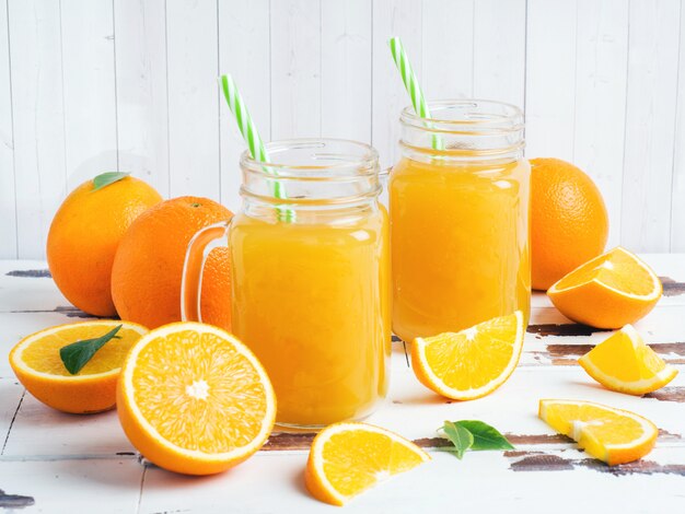 Jus d'orange in glazen potten en verse sinaasappelen op een witte houten rustieke tafel.