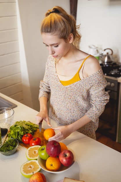 Just attention. Pleased girl standing near table while cutting tomato