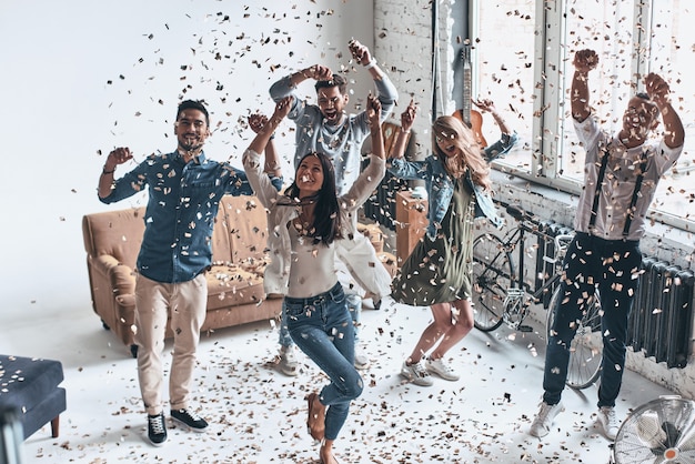 Just feeling happy. Full length top view of happy young people gesturing and smiling while dancing with confetti flying everywhere