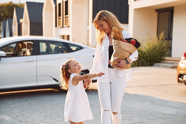 Just from a shopping With bag Young woman with her little daughter is with their electric car outdoors