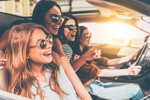 Just keep driving! Side view of four beautiful young cheerful women looking away with smile 