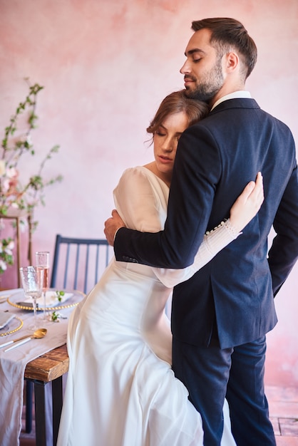 Just married couple hugs. Beautiful bride and groom at the wedding table in the banquet area. Portrait of stylish newlyweds in romantic moment