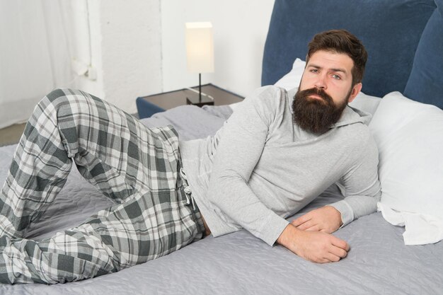 Just one more minute in bed. energy and tiredness. bearded man hipster want to sleep in morning. brutal sleepy man in bedroom. mature male with beard in pajama on bed. asleep and awake. comfort bed.