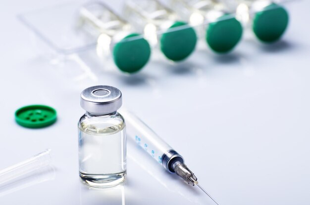 写真 医療テーブルでの注射治療のための注射器と一緒に、ワクチンの準備ができた用量のインフルエンザのショットとして、液体の薬でバイアルを開けただけです。ワクチン接種または予防接種ケアのコンセプトの背景