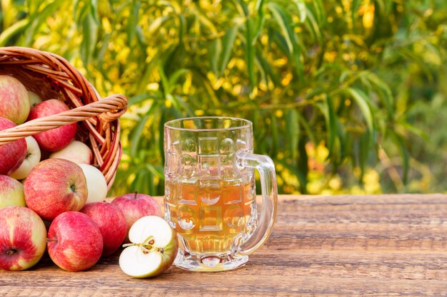 Just picked apples in a wicker basket and apple cider in glass goblet on wooden boards.