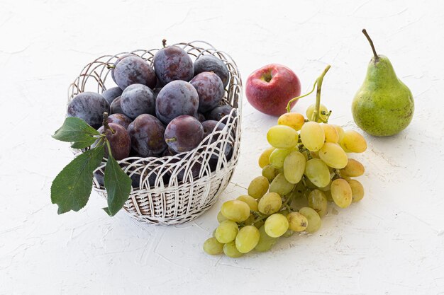 Just picked ripe plums in wicker basket and a bunch of ripe white grapes an apple a pear