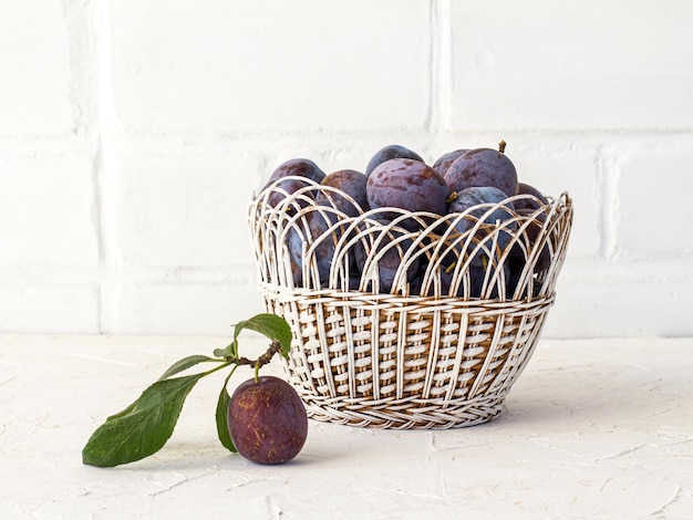 Prugne mature appena raccolte in un cesto di vimini sullo sfondo bianco frutta appena raccolta