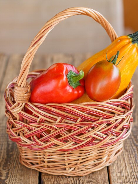 Just picked squash tomatoes and bell pepper in a wicker basket on old wooden boards