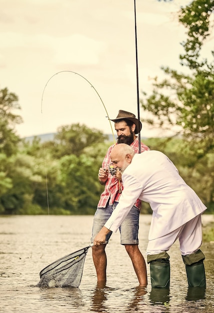 Foto rilassati semplicemente avventure di pesca a mosca papà in pensione e figlio barbuto maturo pescatori felici buon profitto amici uomini con canna da pesca e rete hobby di pesca in pensione uomo d'affari