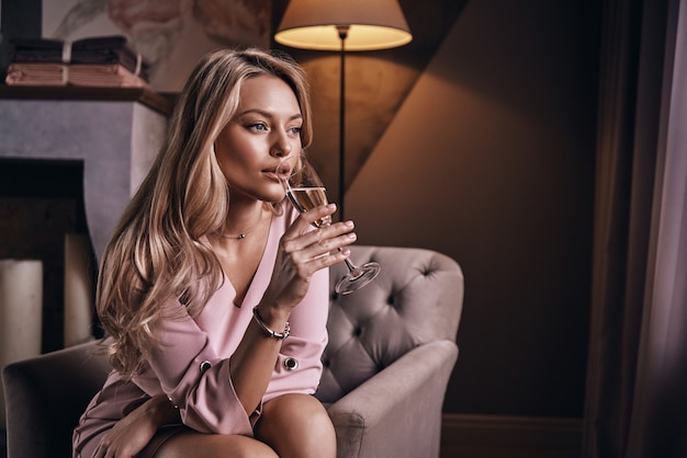 Just relaxing. Attractive young woman drinking champagne while sitting in the armchair