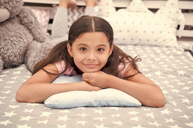 Just relaxing Girl child lay on pillow in her bedroom Kid prepare to go to bed Pleasant time stylish interior Girl kid long hair cute pajamas relaxing on pillow in bedroom Time to sleep or nap