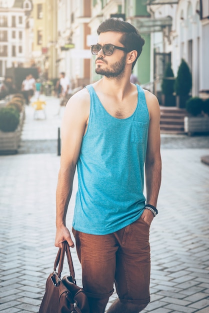 Foto basta andare in giro. bel giovane in abbigliamento casual che trasporta borsa e distoglie lo sguardo mentre si cammina lungo la strada