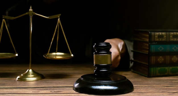 ジャスティス ハンマーと法律の概念小槌真鍮スケール テキスト本で暗い法廷で裁判官はハンマーを保持し、プロの権限の司法決定として有罪の刑事上の公正な法的作業を行います