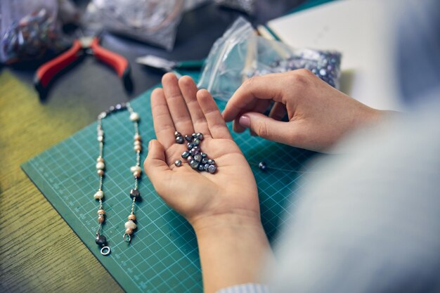 Juwelenmedewerker houdt kralen bij de hand tijdens het kiezen van materiaal voor een ketting