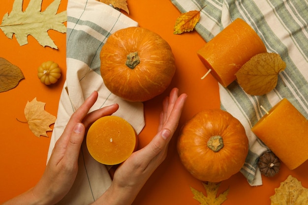 Kaarsen en pompoenen op handdoeken en vrouwelijke handen op oranje achtergrond