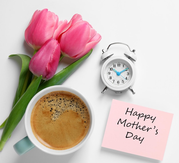 Kaart met zin HAPPY MOTHER39S DAY tulpen kopje koffie en wekker op witte achtergrond plat gelegd