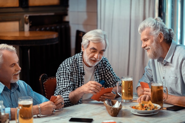 Kaarten en bier. Drie gepensioneerden die aan het kaarten zijn terwijl ze samen bier drinken in de kroeg