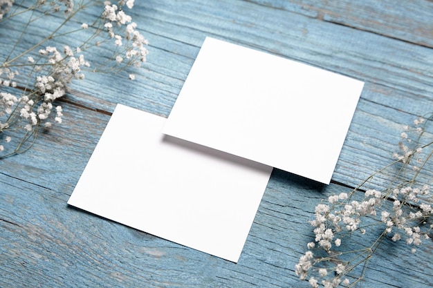 Foto kaartmodel witte lege huwelijksuitnodigingen met bloemendecor op blauwe houten achtergrond