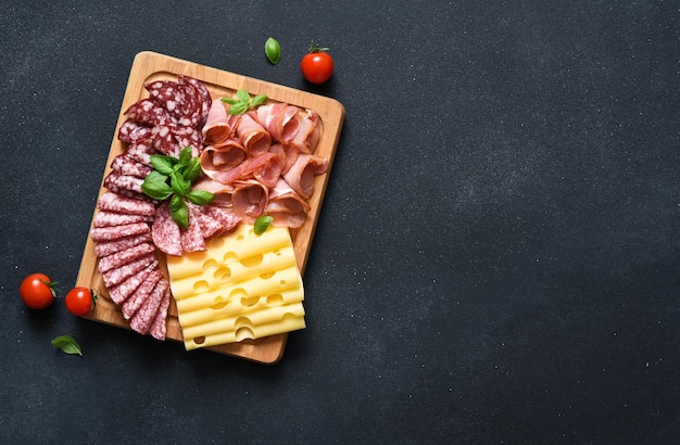 Kaas prosciutto salami op een houten vierkant bord op een zwarte stenen achtergrond