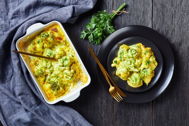 Kaasachtige Broccoli-bak, broccoli-braadpan op een zwarte plaat en in een ovenschaal op een donkere houten tafel, horizontaal zicht van bovenaf, plat gelegd, vrije ruimte