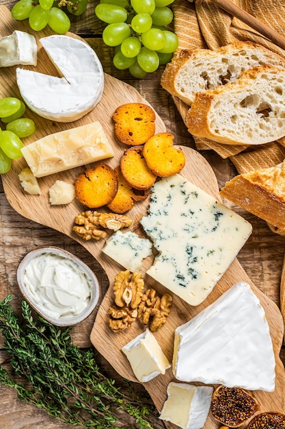 Kaasplankje. Brie, Camembert, Roquefort, Parmezaanse kaas en blauwe roomkaas met druif, vijgen, brood en noten op een houten bord. houten achtergrond. Bovenaanzicht.
