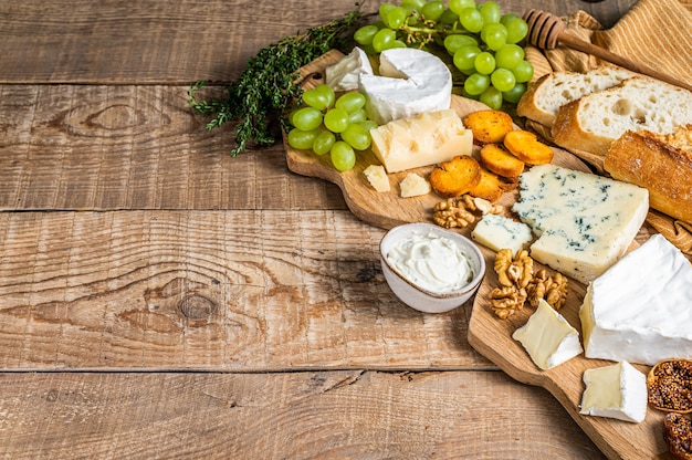 Kaasplankje. Brie, Camembert, Roquefort, Parmezaanse kaas en blauwe roomkaas met druivenmost, vijgen, brood en noten op een houten bord.