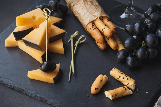 Kaasplankje geserveerd met crackers, druiven en glas witte wijn op donkere achtergrond. Oude Goudse kaas op proefbord