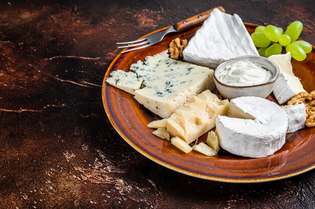 Kaasplankje met Brie, Camembert, Roquefort, blauwe roomkaas, druif en noten. Donkere achtergrond. Bovenaanzicht. Ruimte kopiëren.