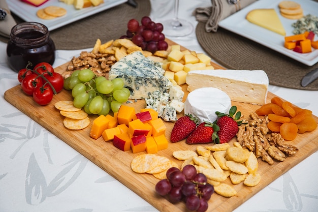 Kaasplankje met verschillende hapjes op tafel. Aardbeien-, abrikozen-, druiven- en graankaasschotels op tafel