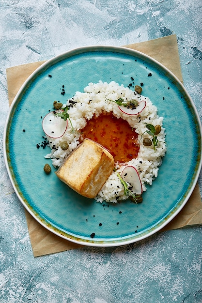 Kabeljauw steak met rijst en saus op een blauwe plaat op betonnen ondergrond.