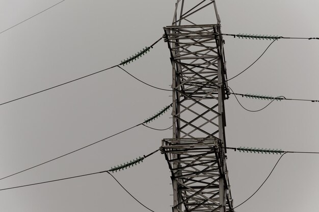 Kabels en modulaire ophangisolatoren voor bovengrondse hoogspanningslijnen Transmissietoren Metalen constructie De lucht in de mist grijze sombere dag Industrie als oorzaak van milieuvervuiling