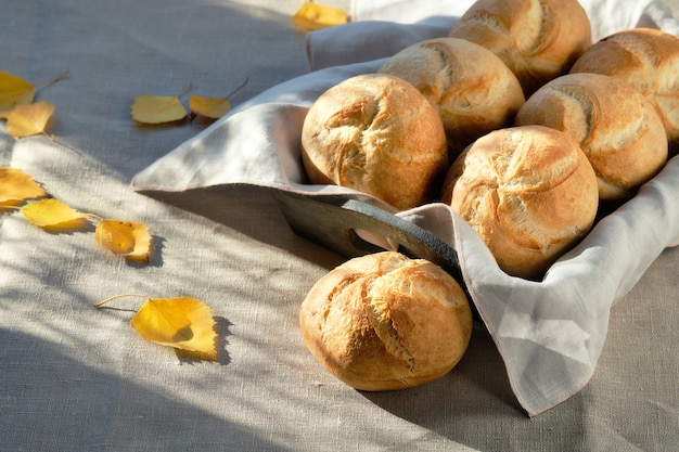 Kaiser- of Weense broodjes in broodmand op textieltafelkleed met gele herfstbladeren.