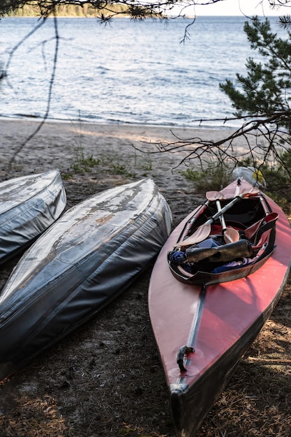 Kajaks liggen aan wal in de schaduw van bomen tegen een zandstrand en meer