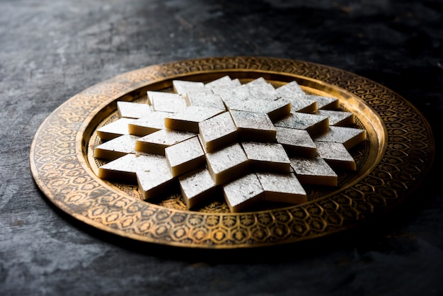 Photo kaju katli is a diamond shape indian sweet made using cashew sugar and mava, served in a plate over moody surface. selective focus