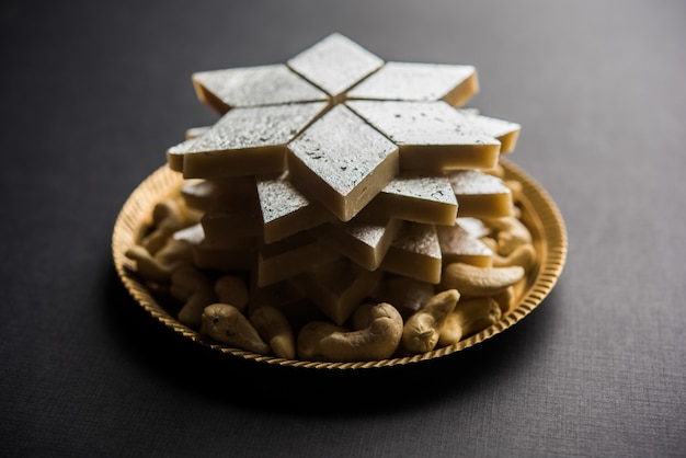 Kaju Katli is een Indiaas snoepje in de vorm van een diamant, gemaakt van cashewsuiker en mava, geserveerd in een bord op een humeurig oppervlak. selectieve focus