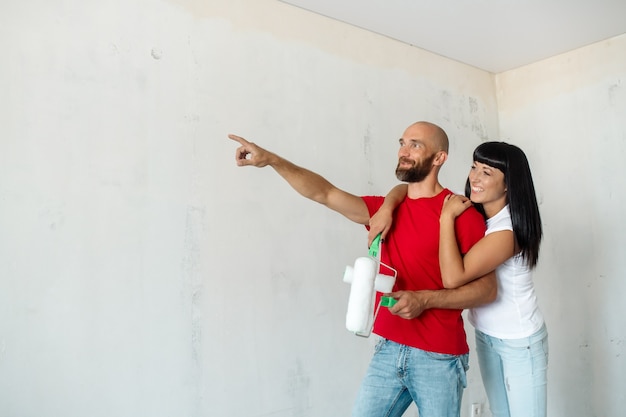 Kale bebaarde jonge man en brunette vrouw schilderen muren thuis met verfroller tijdens renovatie van de kamer