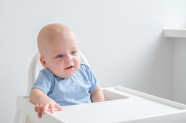 kale glimlachende babyjongen 3 maanden zittend in kinderstoel op witte achtergrond