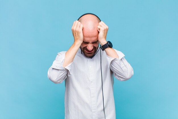 Kale man die zich gestrest en gefrustreerd voelt, zijn hand opheft naar het hoofd, zich moe, ongelukkig voelt en migraine heeft