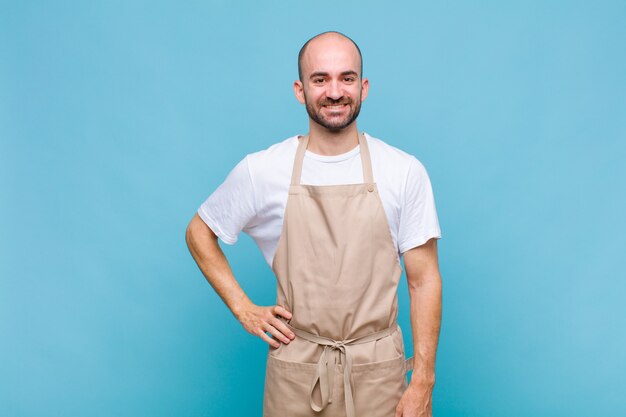 Kale man glimlachend gelukkig met een hand op de heup en zelfverzekerd, positief, trots en vriendelijke houding