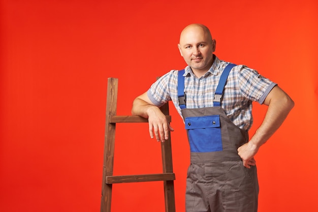 Kale man in werkkleding staat met zijn hand op de ladder