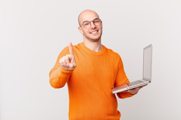 Kale man met computer die trots en zelfverzekerd glimlacht en nummer één triomfantelijk poseert, voelt zich een leider