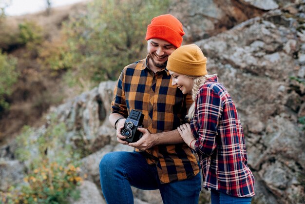 Kale man met een baard en een blond meisje met heldere hoeden op de achtergrond van de rivier maken foto's met een oude camera
