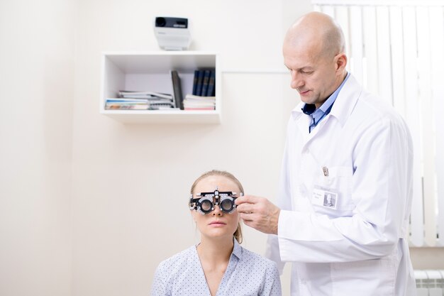 Kale professionele oogarts die gezichtsvermogen van jonge vrouwelijke patiënt onderzoekt om haar individuele lens voor brillen te krijgen
