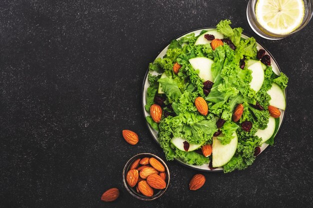 Kale salad with dried cranberry green apples and almonds Vegan healthy food top view black kitchen table