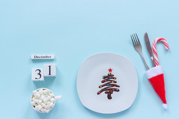 Kalender 31 december. Kerstboom met zoete chocolade op plaat, bestek, kopje cacao