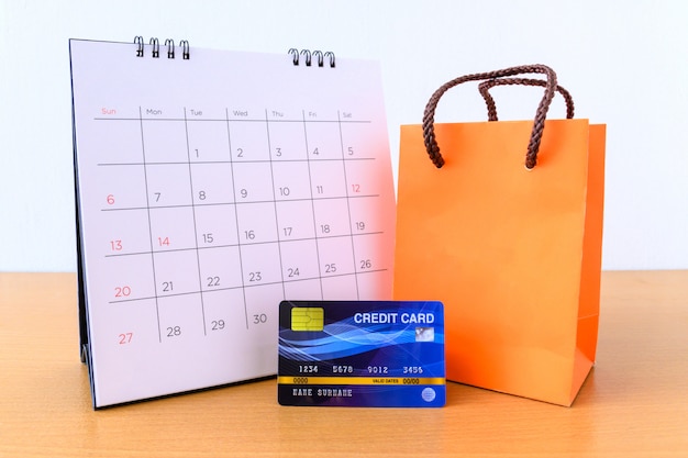 Kalender met dagen en creditcard en oranje papieren zak op houten tafel. winkelen concept