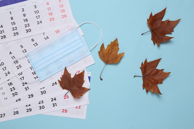 Kalender met gevallen herfstbladeren en een medisch masker op een blauwe achtergrond Herfsttijd Nieuwe realiteit Bovenaanzicht